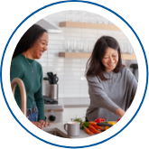 Photo of two women laughing together while one prepares a meal  